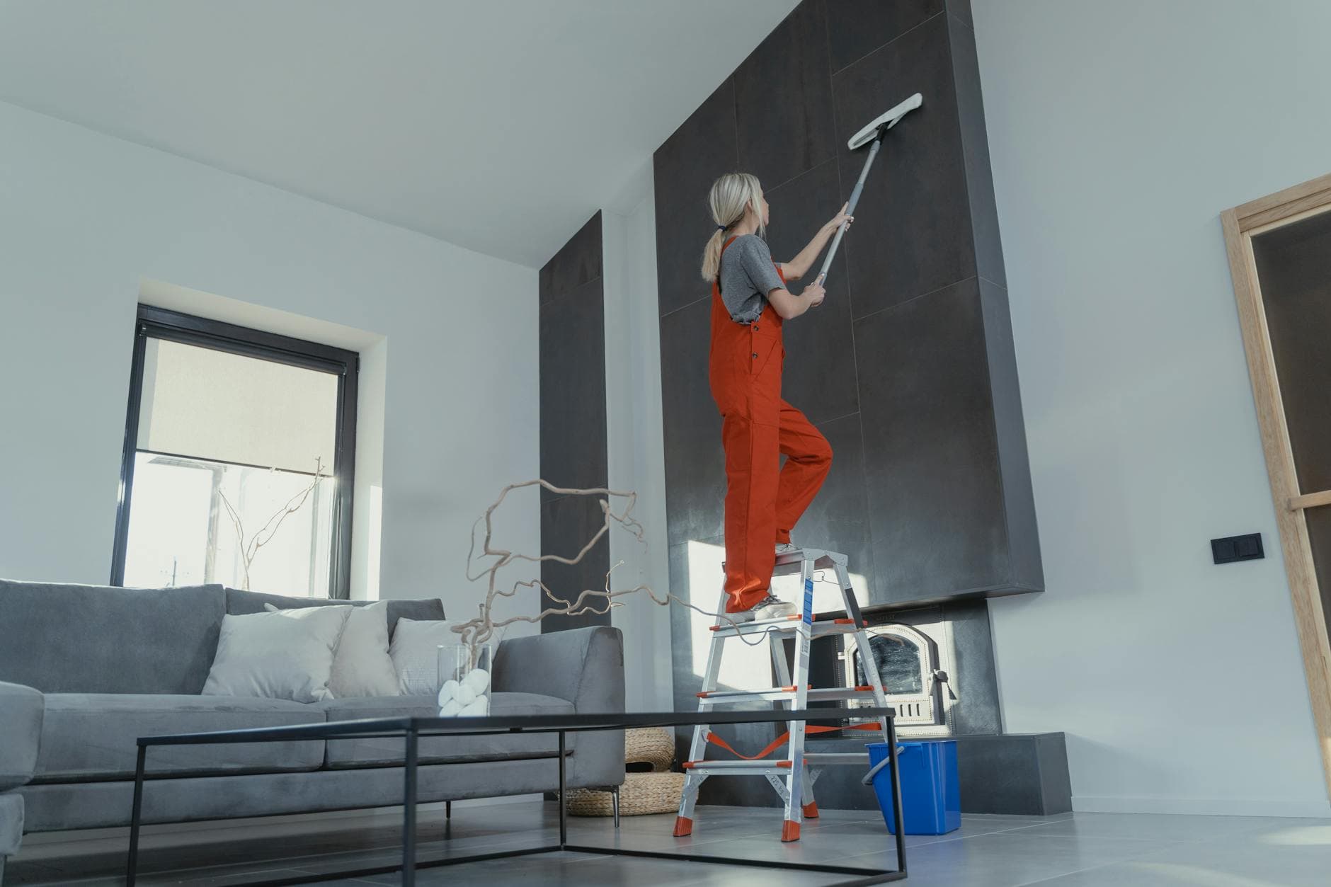 New Jersey Maid cleaner in red overalls on a ladder cleaning a high wall in a New Jersey apartment — hiring in Edison, Central Jersey
