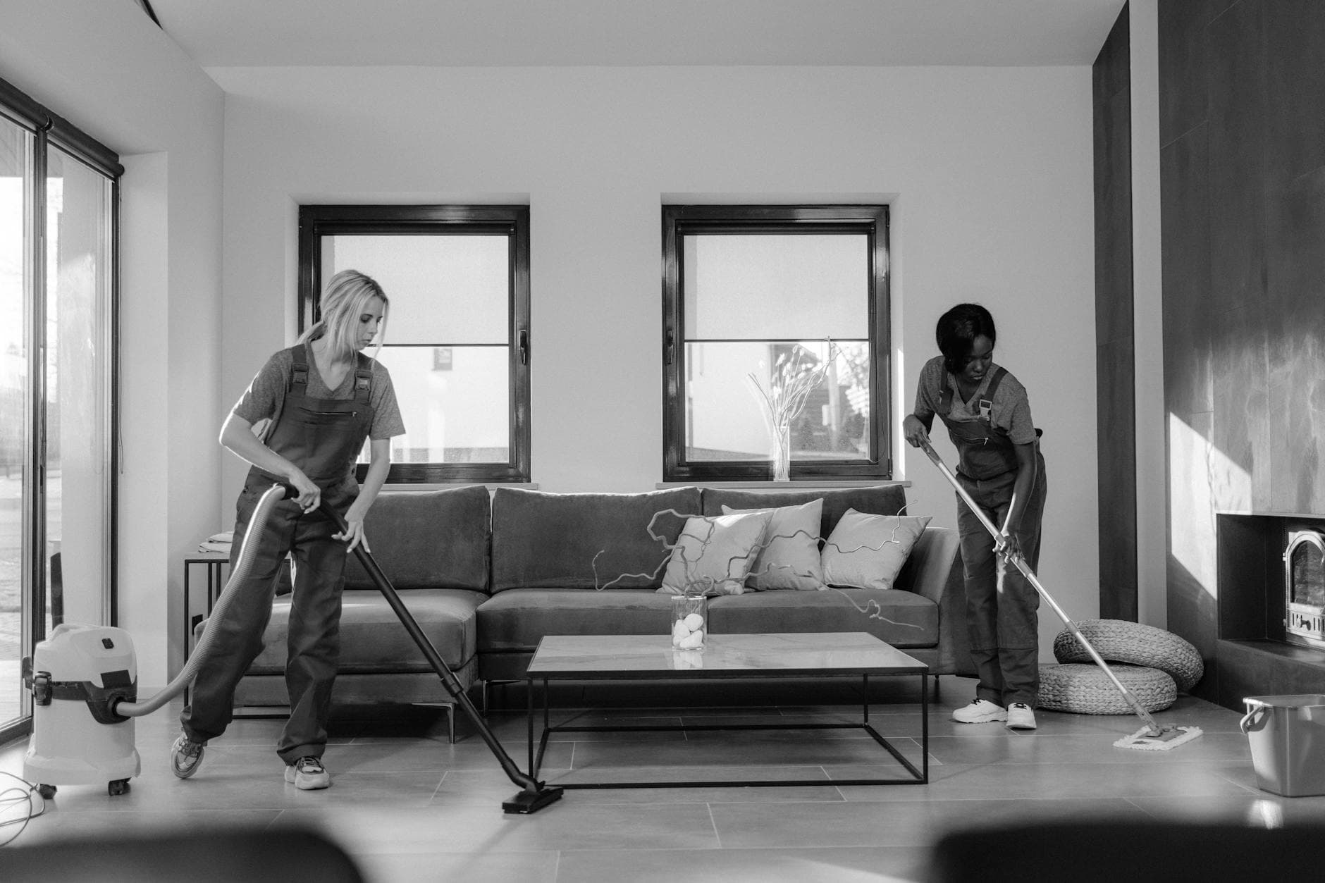 Two New Jersey Maid cleaners in work uniforms using a vacuum and mop in a modern New Jersey living room — Post-Construction Cleanup in North Brunswick, Central Jersey